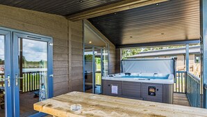 An outdoor patio area with a hot tub, wooden table, and glass doors leading to a deck. - Lakeview 2 Pet Friendly (Woodhall Spa)
