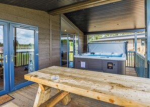 Un patio al aire libre con hidromasaje, una mesa de madera y puertas de cristal que dan a una terraza.