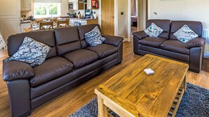 A modern living room with two brown leather sofas, a wooden coffee table, and a kitchen in the background. - Lakeview 2 Pet Friendly (Woodhall Spa)