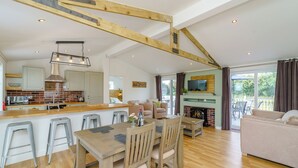 Un vaste espace de vie comprenant une table à manger en bois, des tabourets de bar, un canapé et une cheminée.