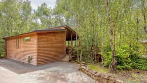 A log cabin with a porch, surrounded by trees and a gravel path. - Cosy log cabin with one double. (Freehay, Cheadle)