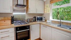 A compact kitchen with a gas stove, oven, microwave, and a window with a view of greenery. - Cosy log cabin with one double. (Freehay, Cheadle)