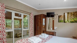 A hotel room with a bed, a TV, a mirror, and a sliding glass door to an outdoor area. - Cosy log cabin with one double. (Freehay, Cheadle)
