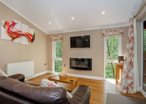 A living room with a brown leather sofa, a wooden coffee table, a flat-screen TV, and a fireplace. - Cosy log cabin with one double. (Freehay, Cheadle)