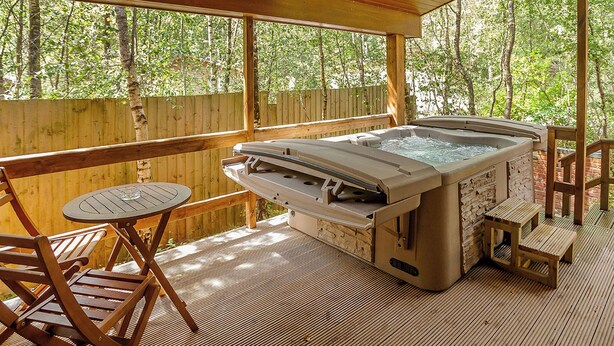 A covered outdoor area with a hot tub, wooden deck, and seating. - Cosy log cabin with one double. (Freehay, Cheadle)
