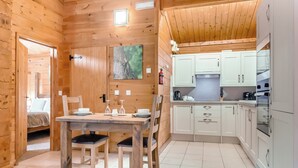 Interior de una cabaña de madera con comedor, cocina y una cama en la habitación contigua.