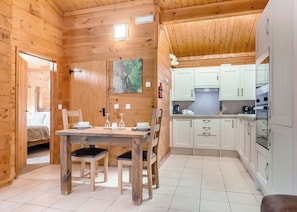 A wooden cabin interior with a dining area, kitchen, and a bed in the adjacent room.