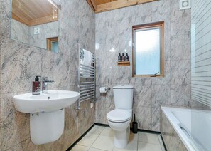 Un baño con lavamanos, inodoro y bañera, paredes de mármol y ventana.