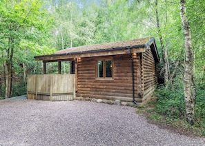 A wooden cabin with a gravel driveway, surrounded by trees.