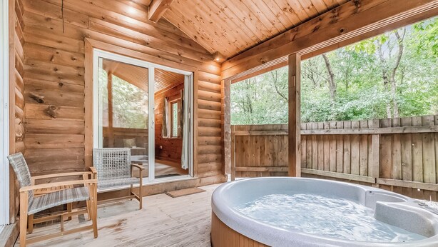 Una cabaña de madera con hidromasaje, sillones de mimbre y vistas al bosque.