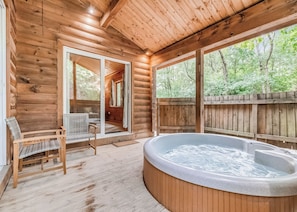 A wooden cabin with a hot tub, wicker chairs, and a view of the forest.