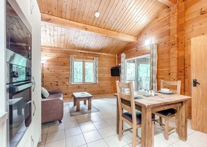 Interior de una cabaña de madera con una mesa de comedor, sillas, un sofá, una mesita y un televisor.