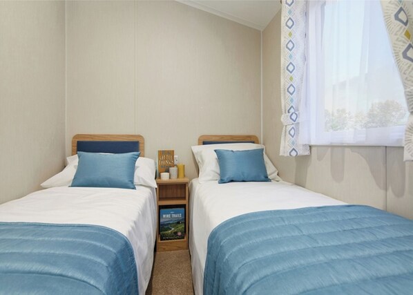 Une chambre double avec deux lits, une table de chevet avec un livre, et une fenêtre avec un rideau à motifs.
