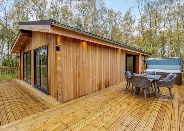 A wooden cabin with a deck, a hot tub, and wicker furniture. - 1 bedroom accommodation in Haddon (Haddon)