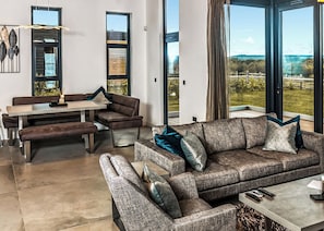 A modern living room with a sofa, bench, dining table, and large windows offering a view of the outdoors. - Four bed lodge with three king-size beds and one twin (king by arrangement). (Nottingham)