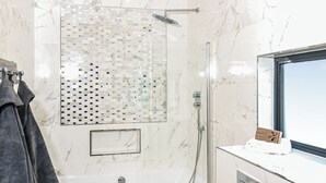 A modern bathroom with a glass-enclosed shower, a marble-tiled wall, a toilet, and a towel rack with a towel. - Four bed lodge with three king-size beds and one twin (king by arrangement). (Nottingham)