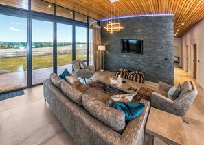 A modern living room with a large sofa, a coffee table, and a flat-screen TV mounted on a stone wall. - Four bed lodge with three king-size beds and one twin (king by arrangement). (Nottingham)