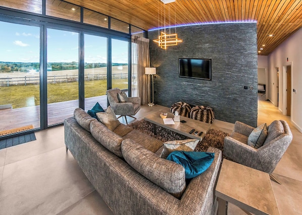 A modern living room with a large sofa, a coffee table, and a flat-screen TV mounted on a stone wall.