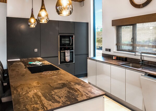 A modern kitchen with a central island, built-in appliances, pendant lighting, and a window providing natural light. - Four bed lodge with three king-size beds and one twin (king by arrangement). (Nottingham)