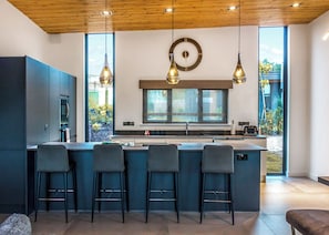 A modern kitchen with a large island, bar stools, pendant lighting, and a clock on the wall.