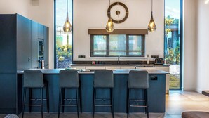 A modern kitchen with a large island, bar stools, pendant lighting, and a clock on the wall. - Four bed lodge with three king-size beds and one twin (king by arrangement). (Nottingham)