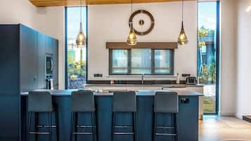 A modern kitchen with a large island, bar stools, pendant lighting, and a clock on the wall.