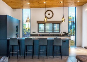 A modern kitchen with a large island, bar stools, pendant lighting, and a clock on the wall. - Four bed lodge with three king-size beds and one twin (king by arrangement). (Nottingham)