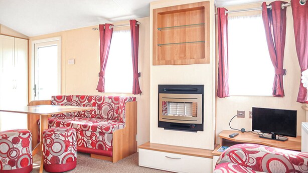 A compact RV interior with a kitchenette, a sofa, a TV, and a small table.