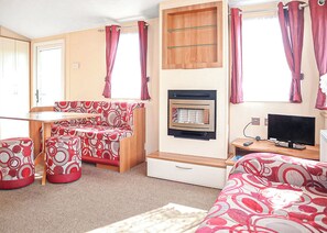 A compact RV interior with a kitchenette, a sofa, a TV, and a small table.