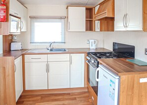 A compact kitchen with a microwave, toaster, sink, stove, and a small refrigerator.