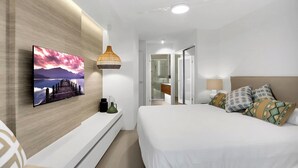 A modern bedroom with a large bed, a mounted TV, a bedside lamp, and a view into the bathroom. - Penthouse 22  - The Cove (Noosa Heads)