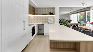 A modern kitchen with white cabinetry, a wooden countertop, and a built-in oven. - Penthouse 22  - The Cove (Noosa Heads)
