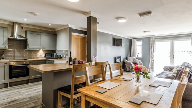 A modern kitchen with a central island, wooden dining table, and chairs. - 1 bedroom accommodation in Crimdon (Crimdon)