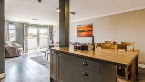 A modern kitchen with a central island, a dining area with wooden chairs, and a view through a glass door to the outside. - 1 bedroom accommodation in Crimdon (Crimdon)