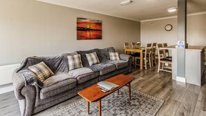 A living room with a sofa, a coffee table, a dining table with chairs, a painting on the wall, and a clock. - 1 bedroom accommodation in Crimdon (Crimdon)