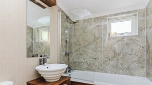 Un bagno con una parete in marmo, un mobile vanitario in legno, un lavandino bianco, una vasca e uno specchio.