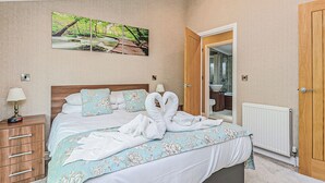 Una camera da letto con un letto, un comodino, una lampada, un quadro e un bagno visibile attraverso una porta aperta.