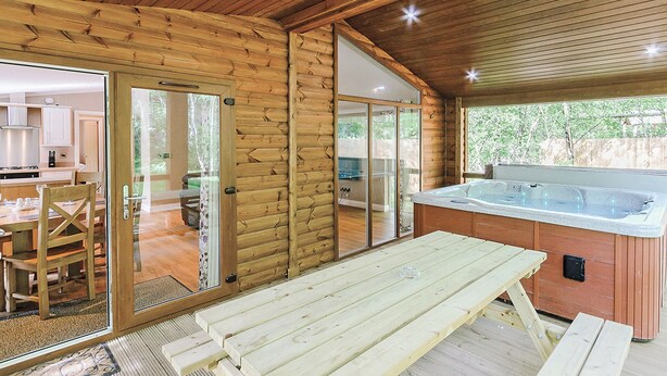 Interno di una baita in legno con zona pranzo, porte scorrevoli in vetro e vasca idromassaggio.