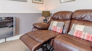 A brown leather sofa with a reclining mechanism, a plaid pillow, and a lamp on a side table.