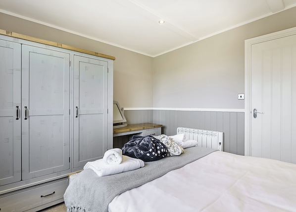 Un dormitorio con cama, armario, radiador y escritorio.