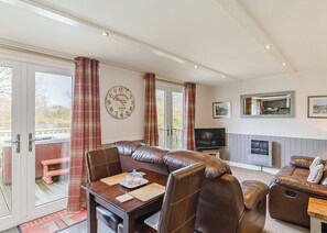 A room with a leather sofa, a dining table with cutlery, a television, and a clock on the wall. - Luxury lodge with one double, ideal for couples. (Pickering)