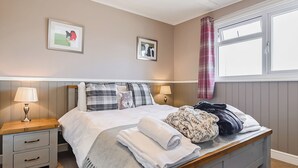 A neatly made bed with pillows, a bedside table with a lamp, and a window with curtains.
