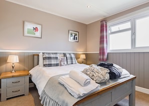 A neatly made bed with pillows, a bedside table with a lamp, and a window with curtains.