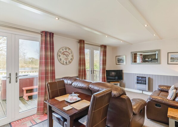 A room with a leather sofa, a dining table with cutlery, a television, and a clock on the wall.