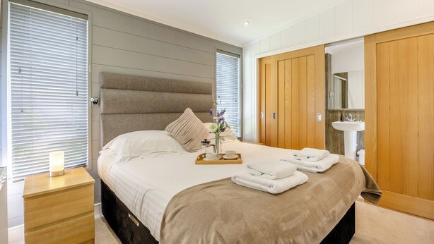 A hotel room with a large bed, bedside table, wooden wardrobe, and a bathroom with a sink and mirror. - Lakeview Premier Pet Friendly (Woodhall Spa)