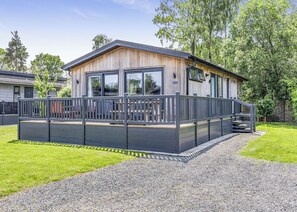 Une cabane moderne en bois, dotée d’une terrasse, de grandes fenêtres et d’une allée en gravier.