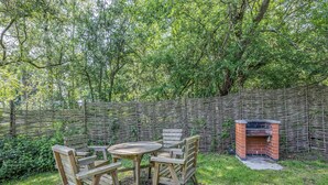 A wooden outdoor seating area with a brick barbecue grill, surrounded by lush greenery and a woven fence. - Lakeview Premier Pet Friendly (Woodhall Spa)