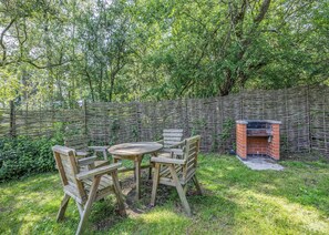 Un espace extérieur aménagé avec des sièges en bois, un barbecue en briques et entouré d’une végétation luxuriante, le tout délimité par une clôture en osier.