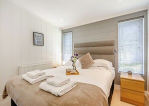A neatly made bed with towels, a bedside table with a clock, and a framed quote on the wall. - Lakeview Premier Pet Friendly (Woodhall Spa)