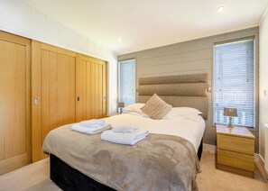 Une chambre à coucher avec un grand lit, une armoire en bois, des tables de chevet et une fenêtre avec des stores.